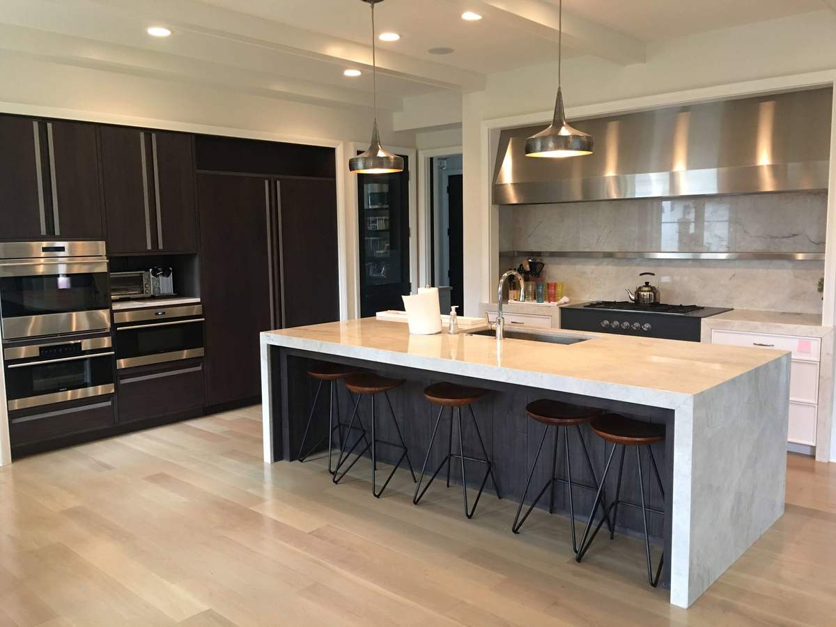 Kitchen island with stools, dark cabinets, and stainless range hood